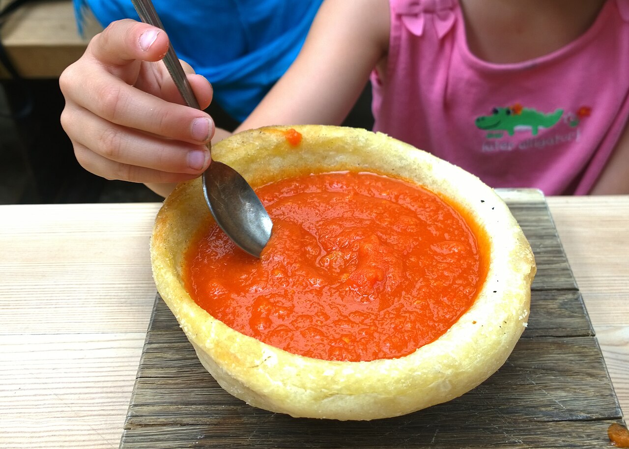 A tomato bisque served in a shallow cup &mdash; the castle banquet uses the same no-spoon geometry so you drink it one-handed between fights.